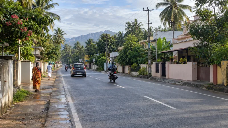 Tree-lined urban-edge road in Chunkankadai with homes, local traffic and Western Ghats foothills