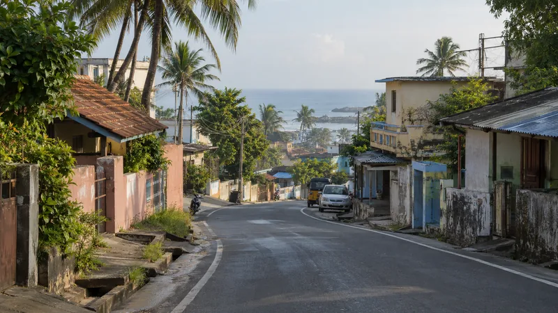 Coastal neighbourhood road in Colachel with modest homes, coconut palms and the Arabian Sea