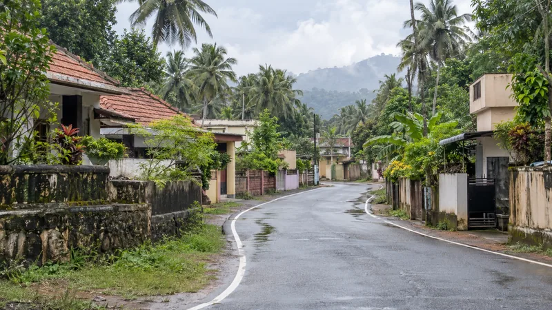 Rain-washed residential street in Karungal with tiled homes, tropical greenery and distant low hills