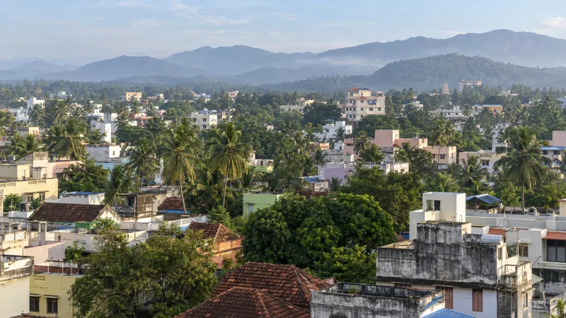 Elevated view across Marthandam's tropical townscape with homes, coconut trees and distant Western Ghats